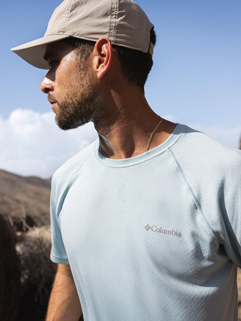 Man wearing light blue t-shirt and tan baseball cap outdoors, shown in profile view.
