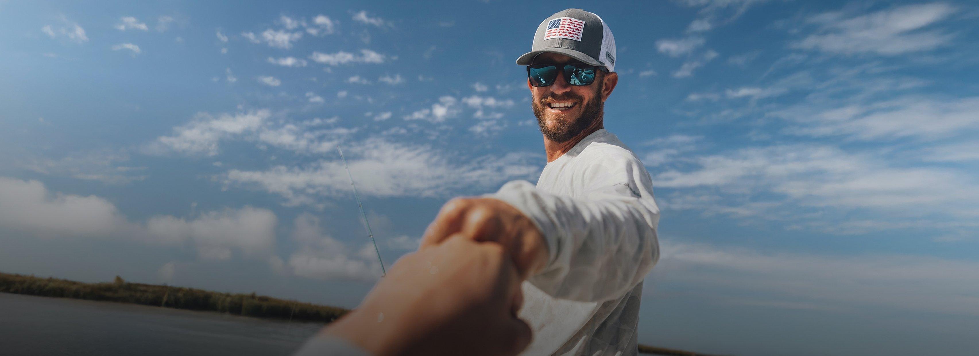 Man fishing outdoors wearing gray and white cap with American flag patch and blue mirrored sunglasses.