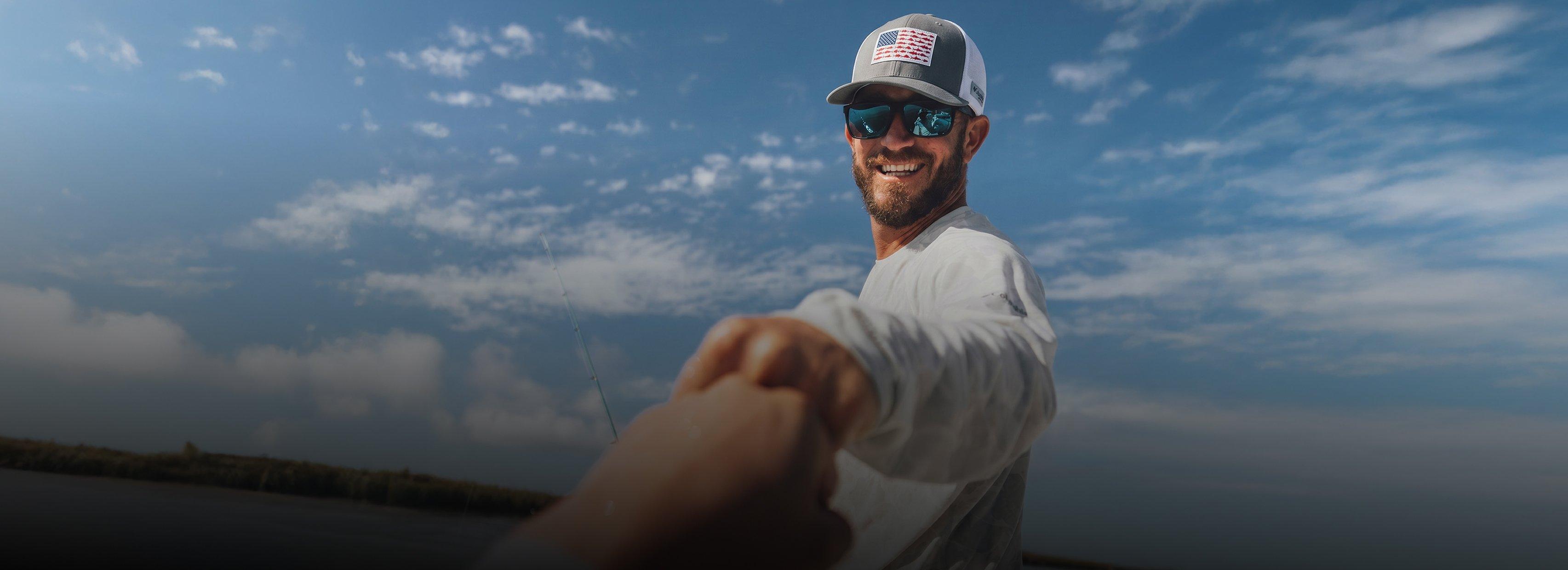 Man fishing outdoors wearing gray and white cap with American flag patch and blue mirrored sunglasses.