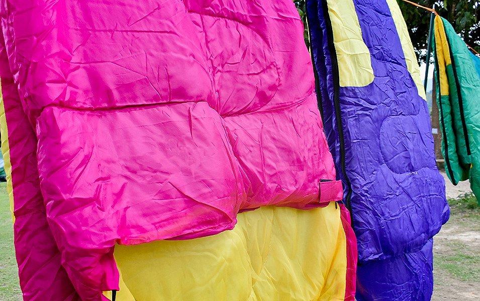 Several colorful sleeping bags are draped over a clothesline outdoors.