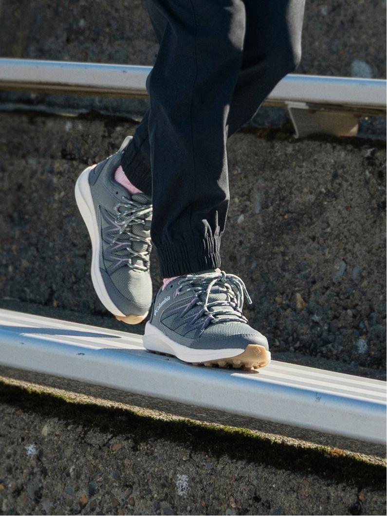 Person walking on wooden plank wearing gray and pink athletic sneakers with black pants.