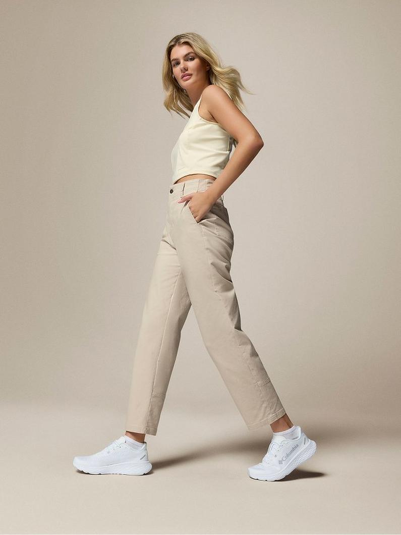 Model walking in cream crop top, beige pants, and white sneakers with hand in pocket.
