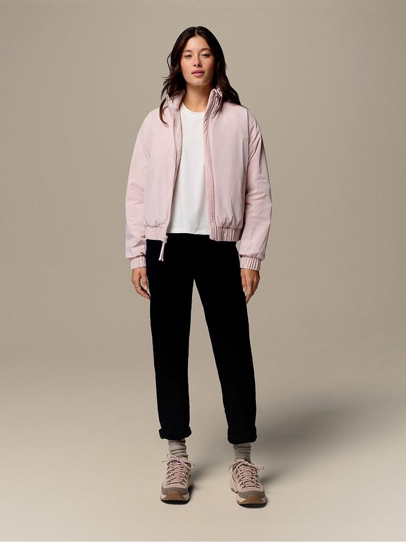 Woman wearing light pink bomber jacket over white top with black pants and beige sneakers.