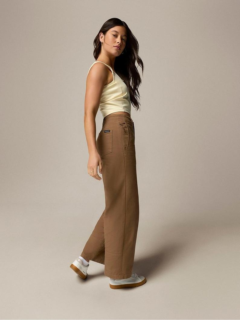 Woman wearing pale yellow cropped cami top with brown wide-leg pants and white sneakers, standing in profile.