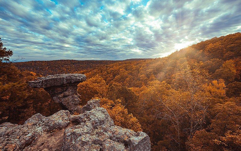 A prominent flat-topped outcrop rises above a hardwood forest with orange foliage.