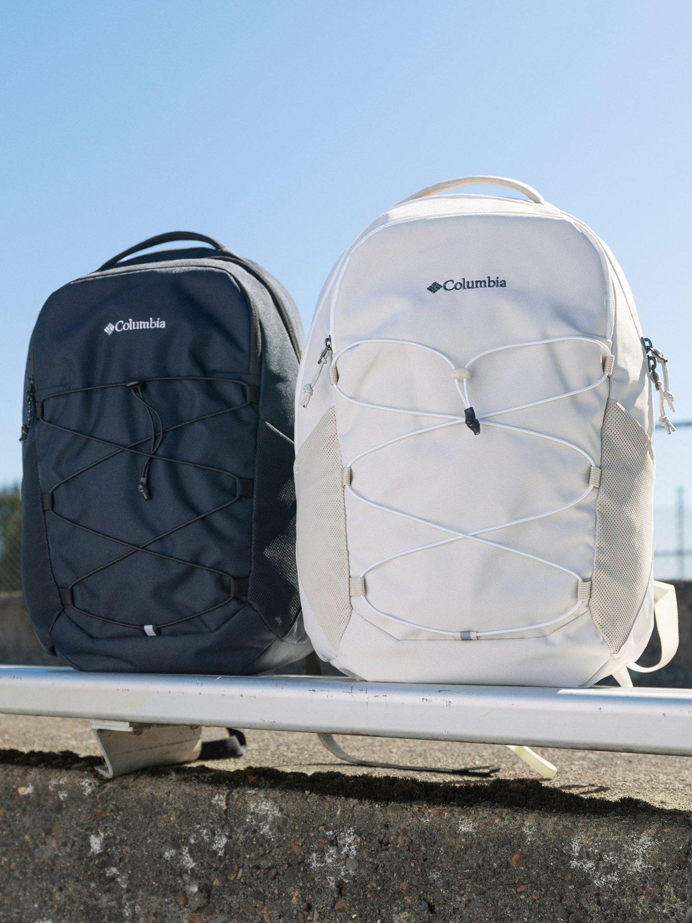 Two backpacks in black and white with elastic cord detailing on front, positioned on a metal railing.