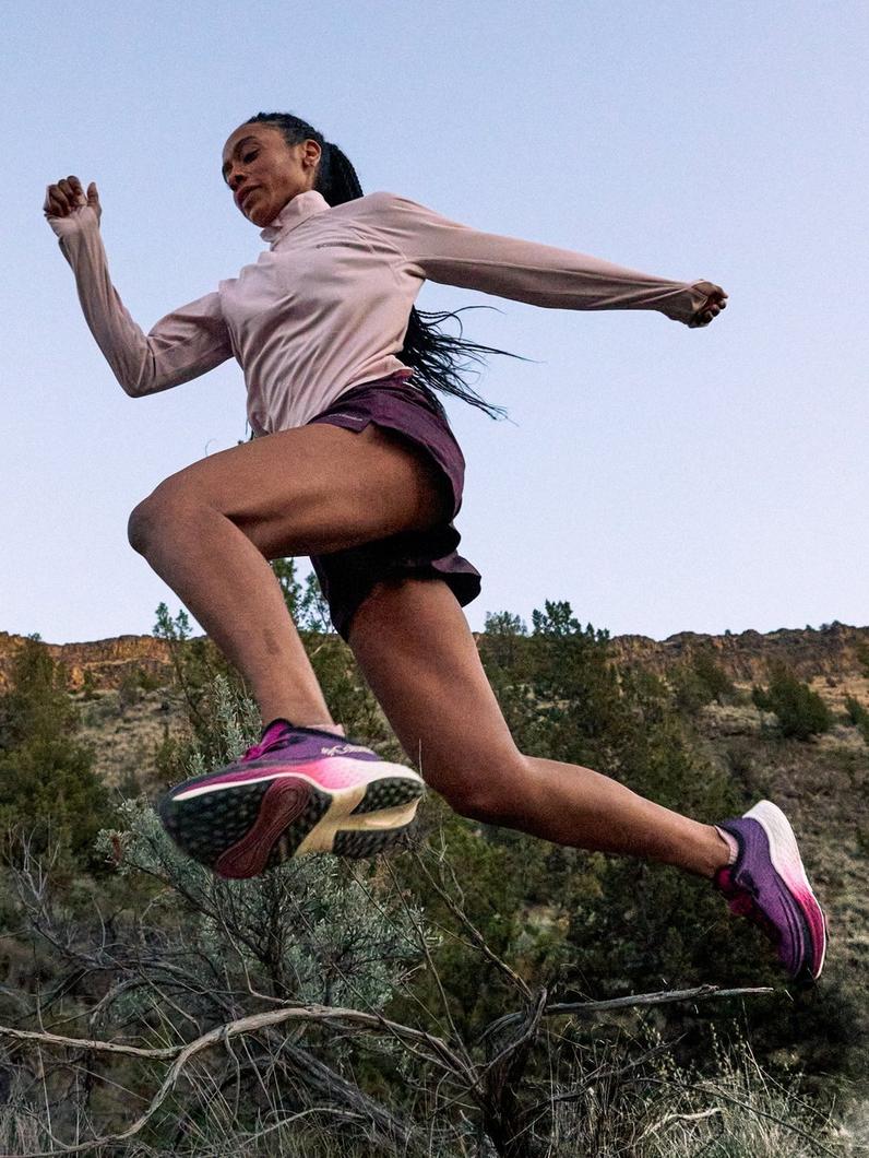 Woman running outdoors in purple athletic shoes and shorts with white long-sleeve top.
