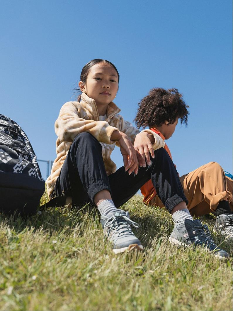 Children sitting on grass wearing athletic sneakers and casual sportswear on a sunny day.