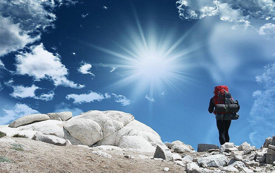 A hiker with a large red backpack, tent, and sleeping pad strapped underneath walks through a boulder field of white granite.