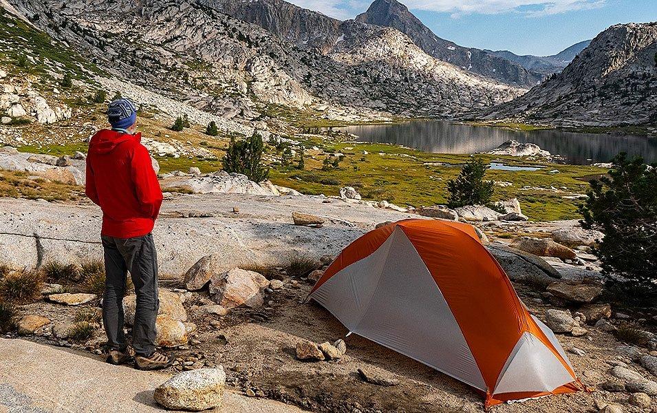 A solo camper has pitched a small tent by an alpine lake.