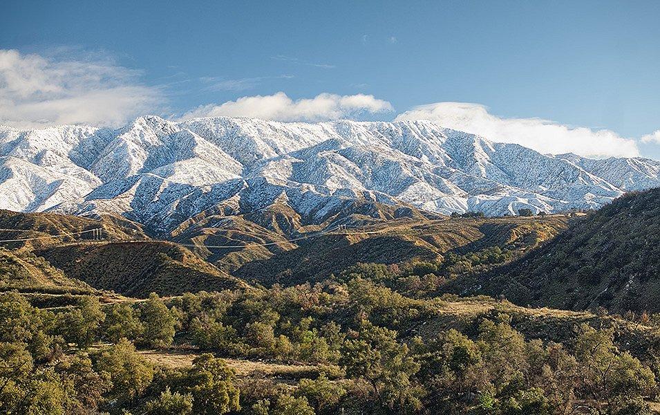 Snow-covered mountains give way to greener foothills and tree-covered valleys.