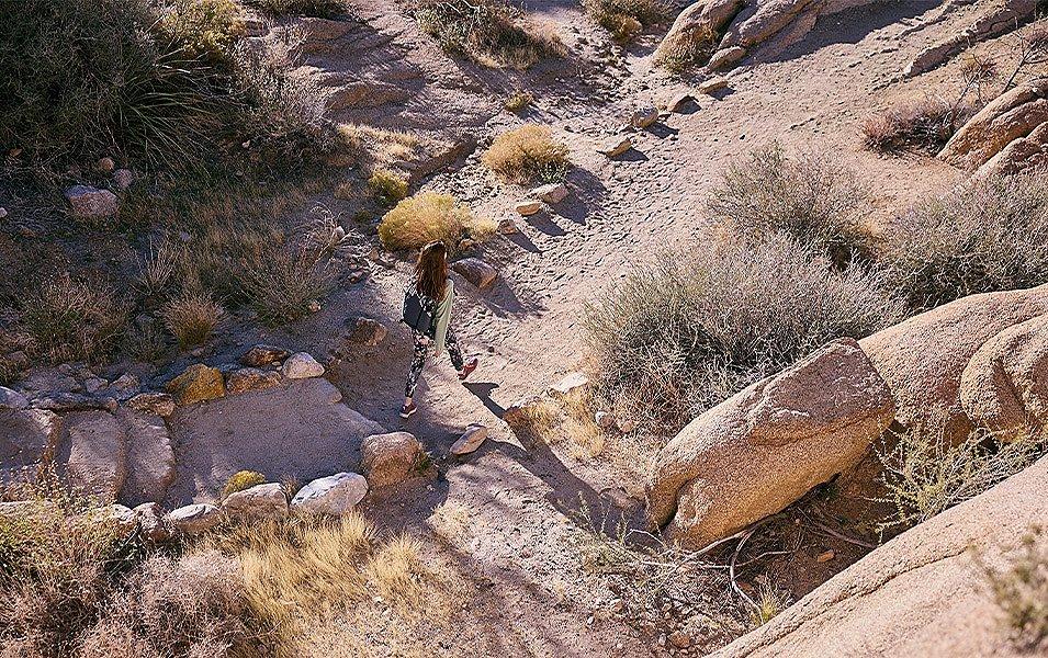 A woman strolls down a sandy trail through a boulder field.