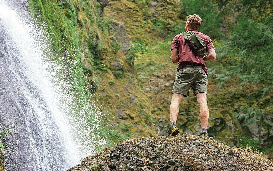 A man with a backpack looks up at a waterfall.