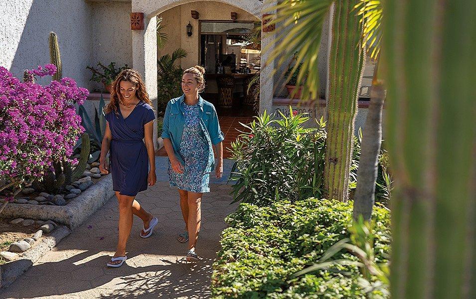 Two people laugh as they walk out onto a sunny courtyard.
