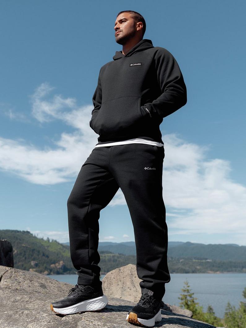 Man standing on rocky outcrop wearing black hoodie and matching joggers with athletic shoes.