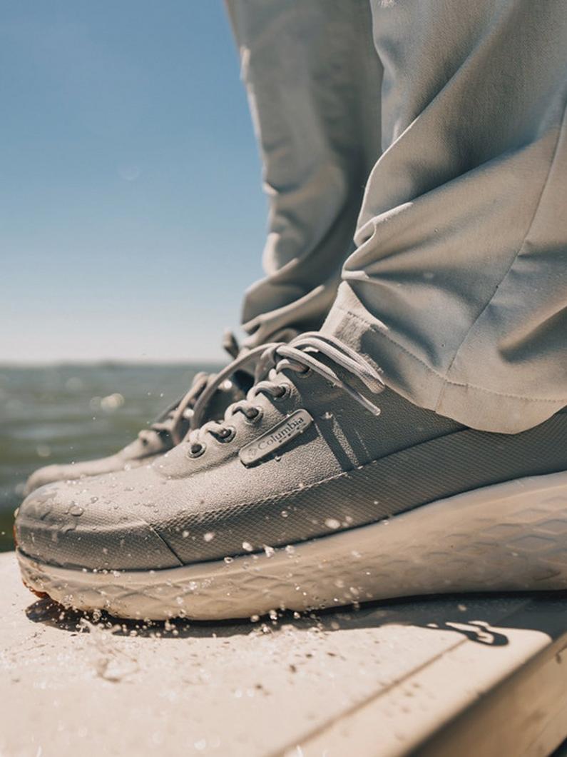 Person wearing gray lace-up sneakers and pants walking on wet surface with water splashing.