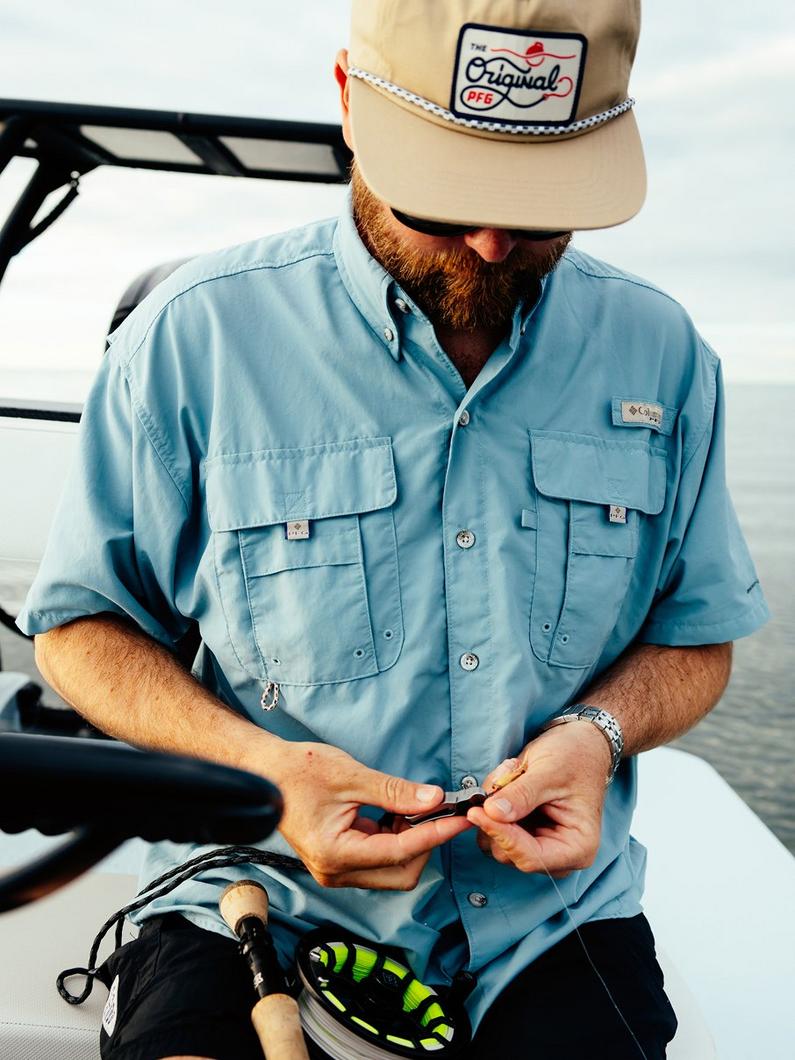 Man wearing light blue fishing shirt with chest pockets, tying fishing line on a boat.