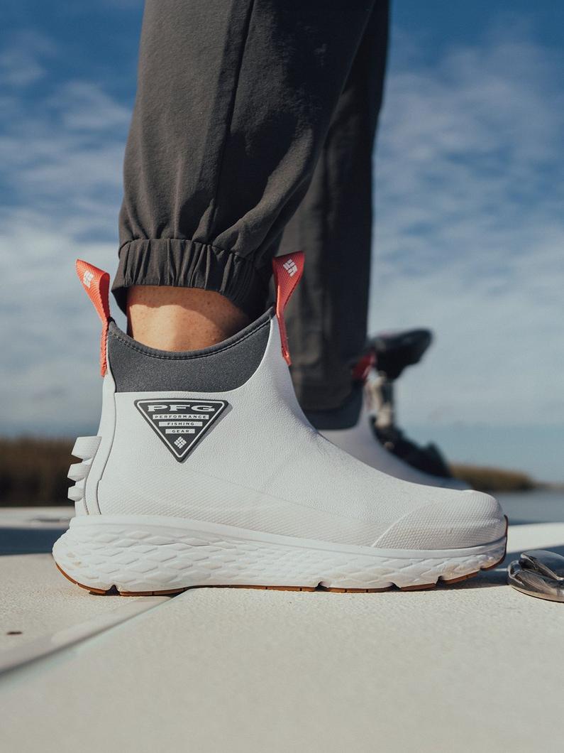 White waterproof ankle boot with orange pull tabs and PFG logo, worn with gray joggers on boat deck.