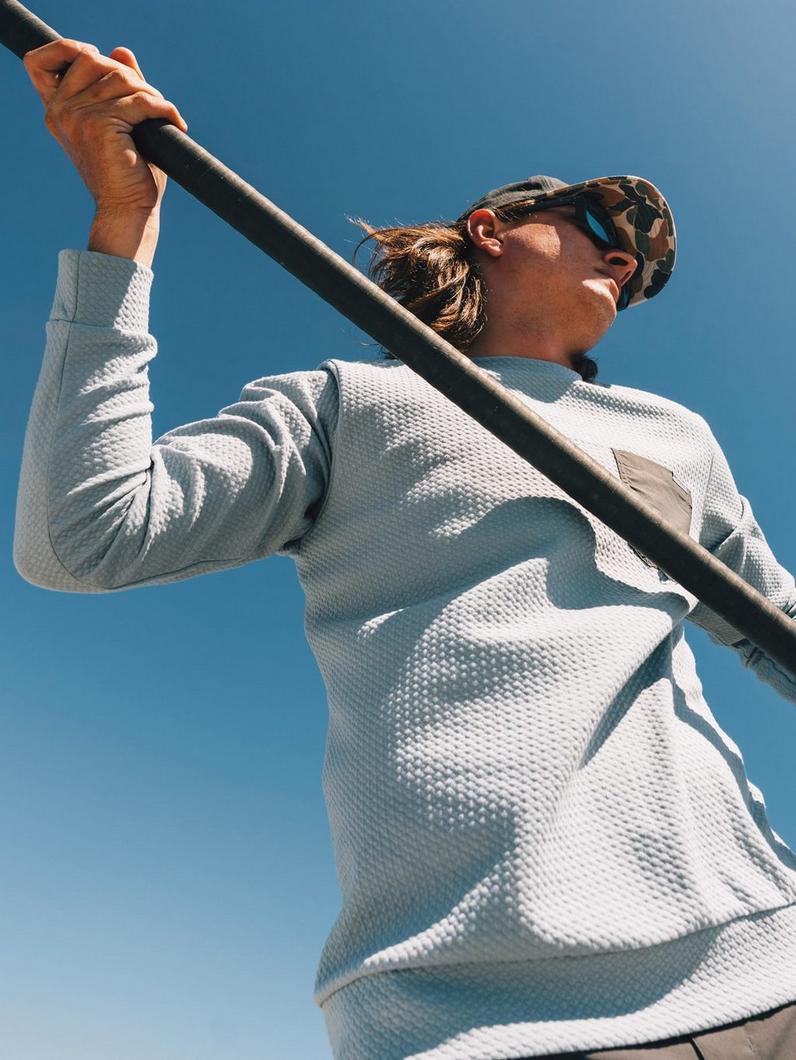 Woman in white textured pullover and camouflage cap holding paddle while kayaking outdoors.