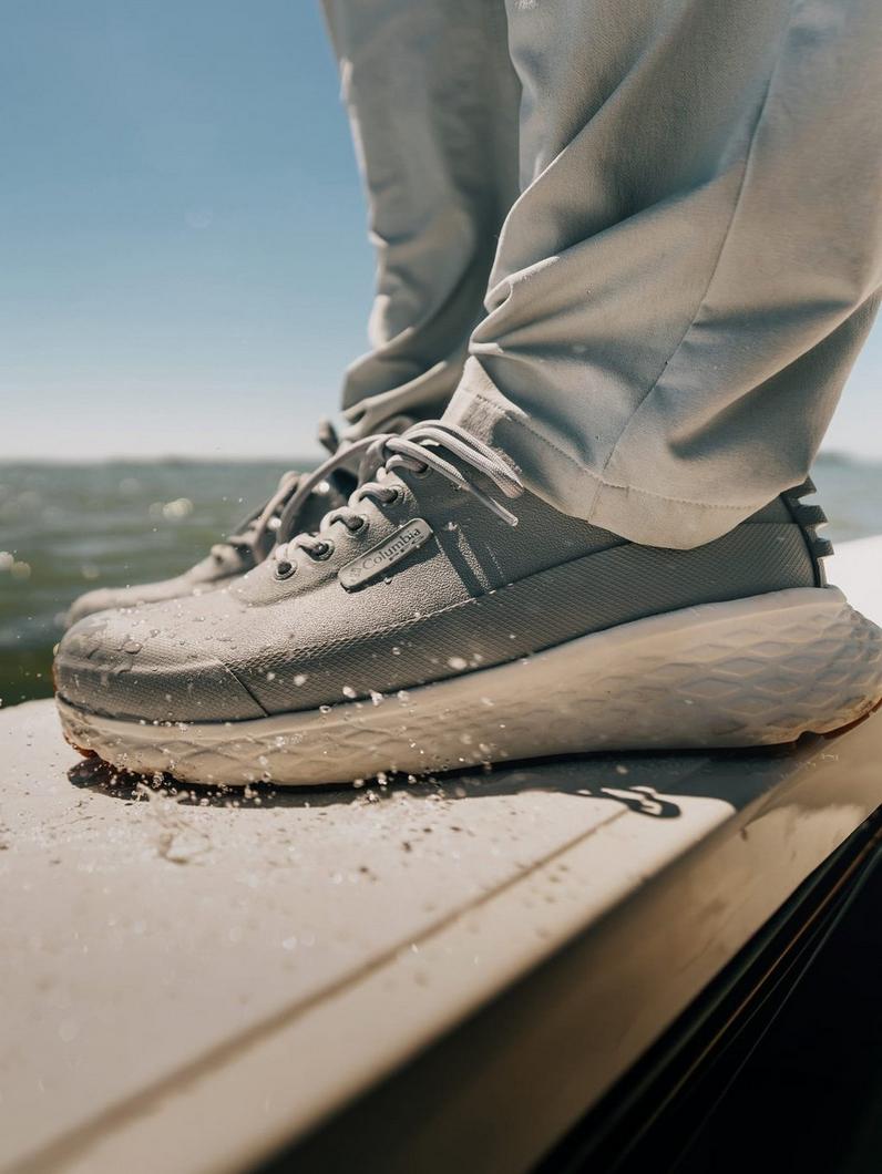 Person wearing gray athletic sneakers stepping on wet boat deck with water splashing around the sole.