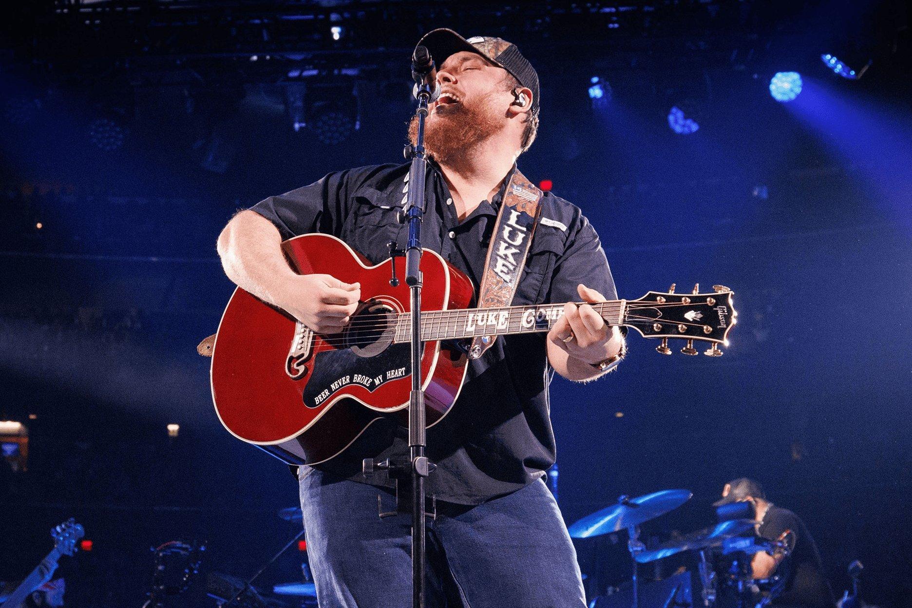 Musician performing live on stage, singing and playing red acoustic guitar with microphone.