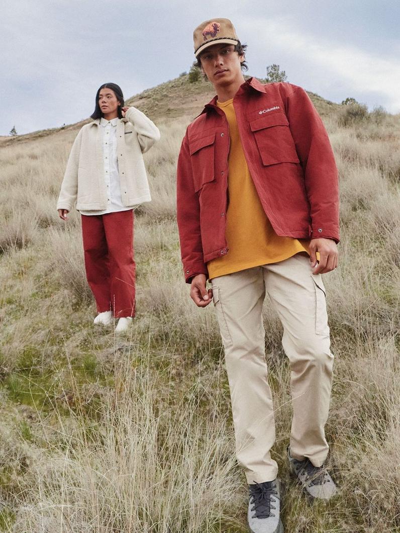 Two people hiking outdoors wearing casual outerwear jackets and pants in autumn colors.