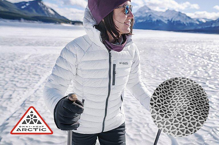 Omni Heat Arctic logo. Woman wearing an Arctic Crest hooded jacket in the snow. 