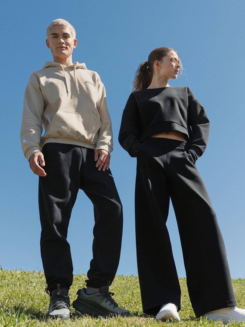 Two models standing outdoors wearing casual athletic wear, including hoodies and black sweatpants.
