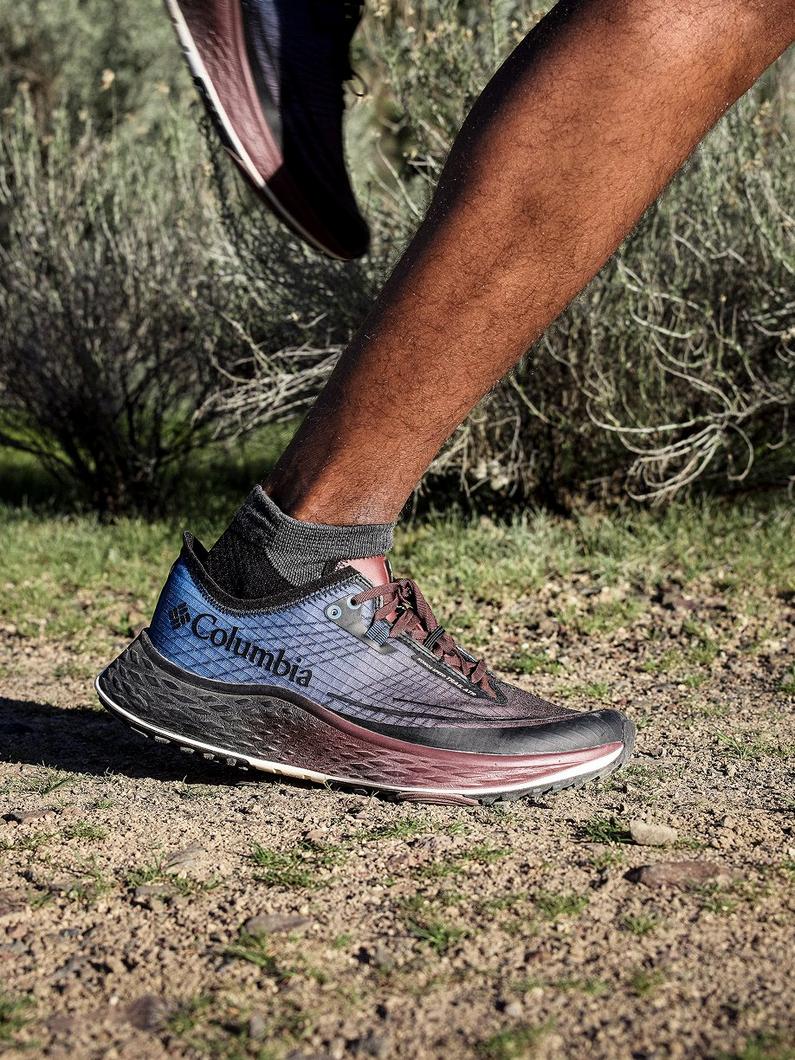 Person walking on outdoor trail wearing blue and brown athletic hiking shoe with gray sock.