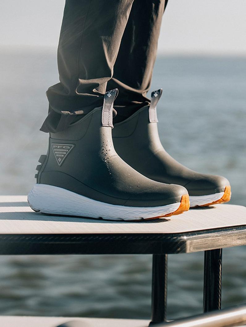 Person wearing waterproof ankle boots with white soles and orange treads, standing on a boat deck.