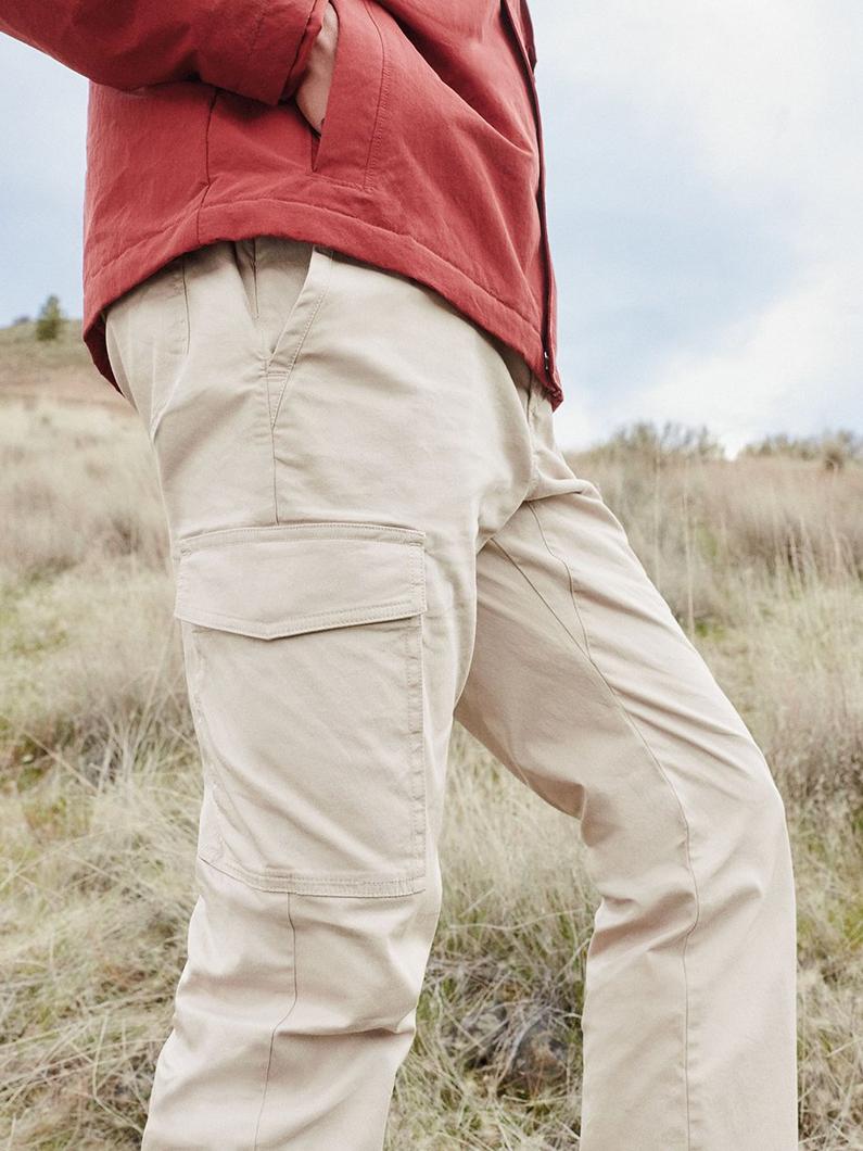 Person wearing beige cargo pants with side pocket and coral jacket standing outdoors in natural setting.