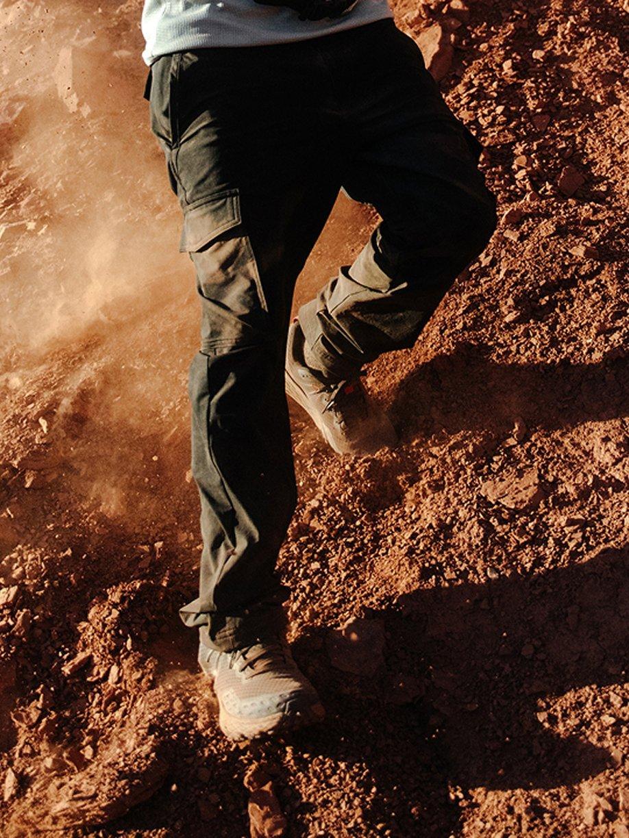 Man scrambling down a rugged trail, kicking up dust.