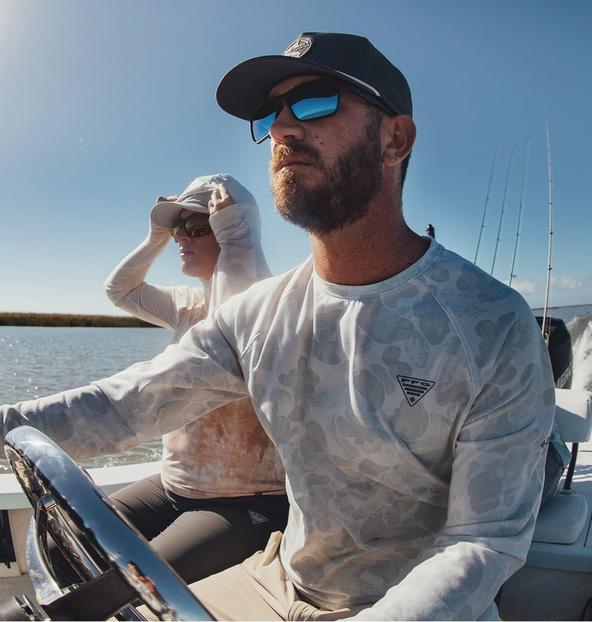 Man wearing light gray camouflage long-sleeve shirt and sunglasses while fishing on a boat.