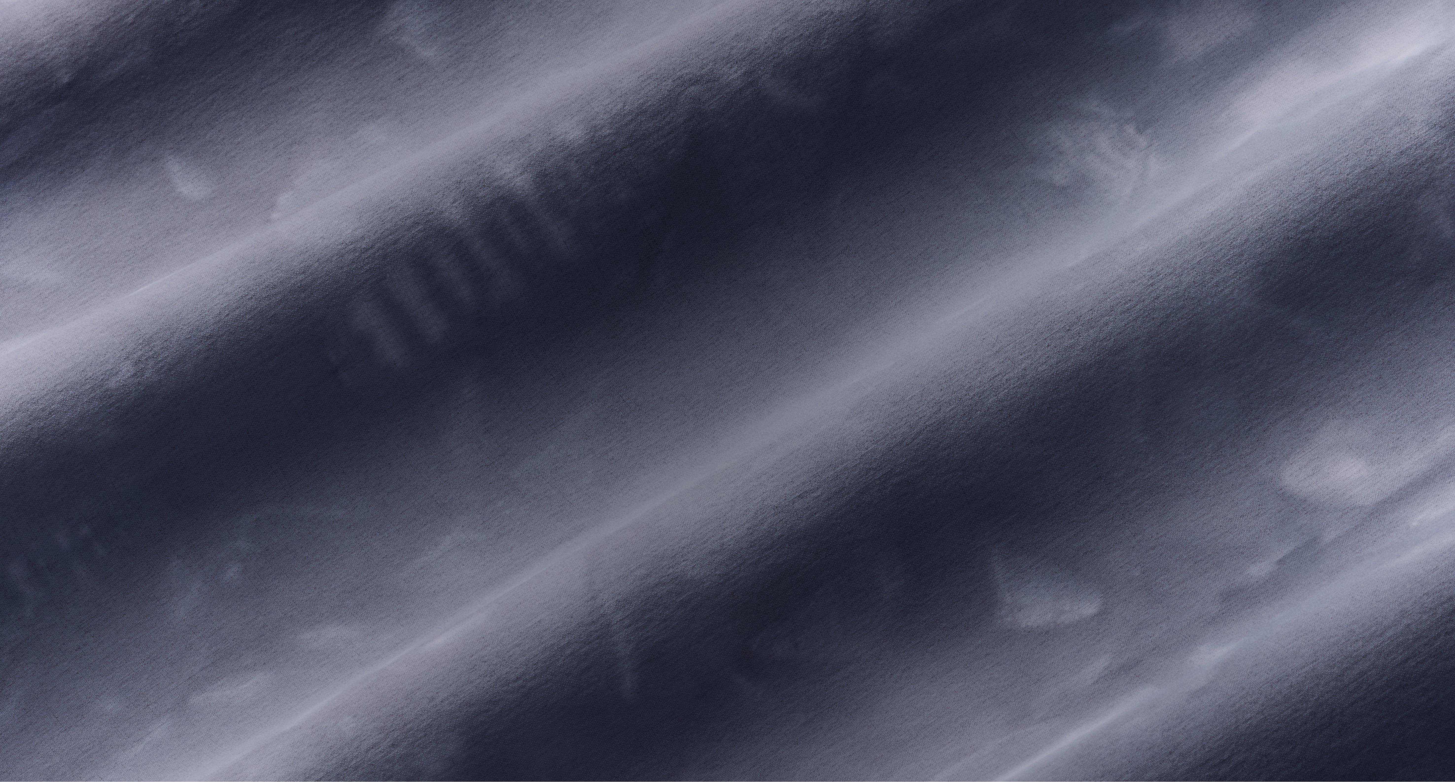 Close-up of smooth fabric with soft diagonal folds in blue-gray tones creating a textured surface.