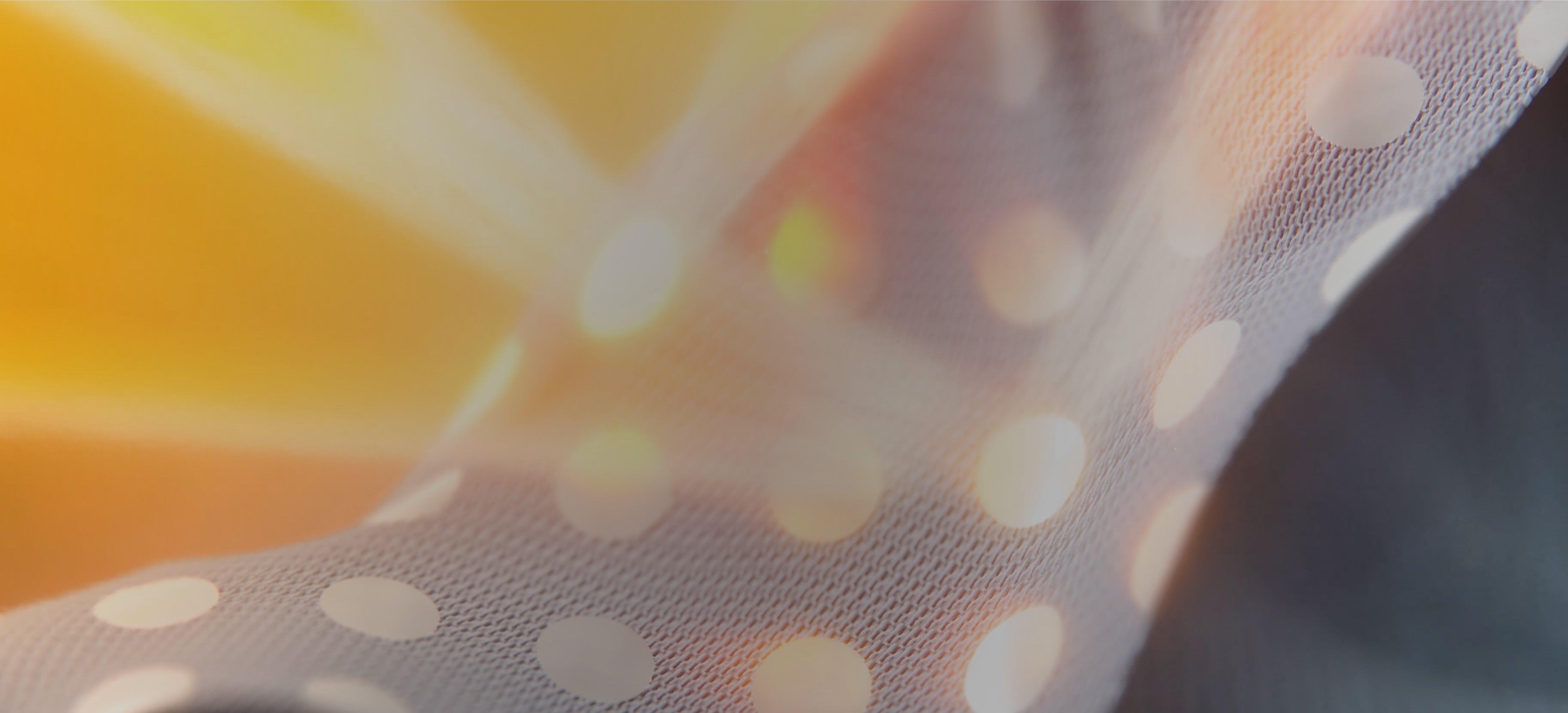 Close-up of gray fabric with white polka dots, softly illuminated by warm sunlight.