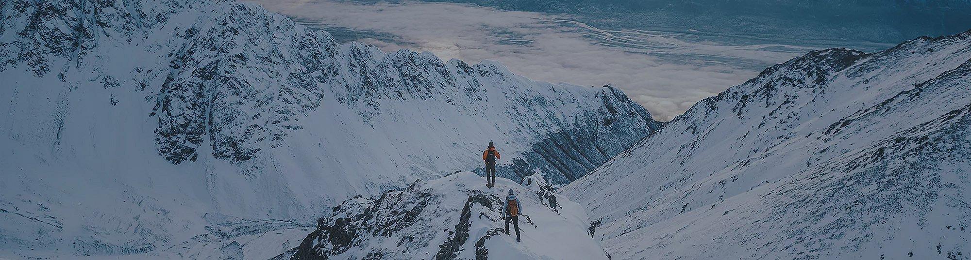  Two people in Columbia gear hiking in a snow-covered mountain range. 