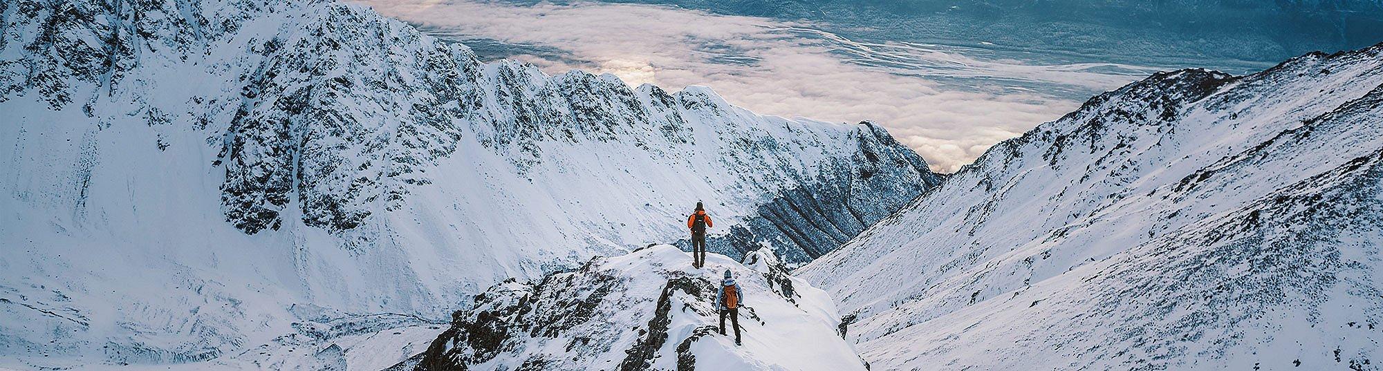 Two people in Columbia gear hiking in a snow-covered mountain range. 