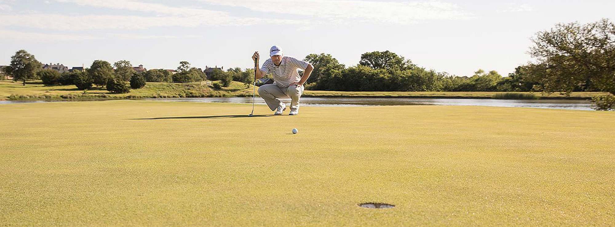 Golfer crouching down plan his next shot with a golf ball close to the hole.