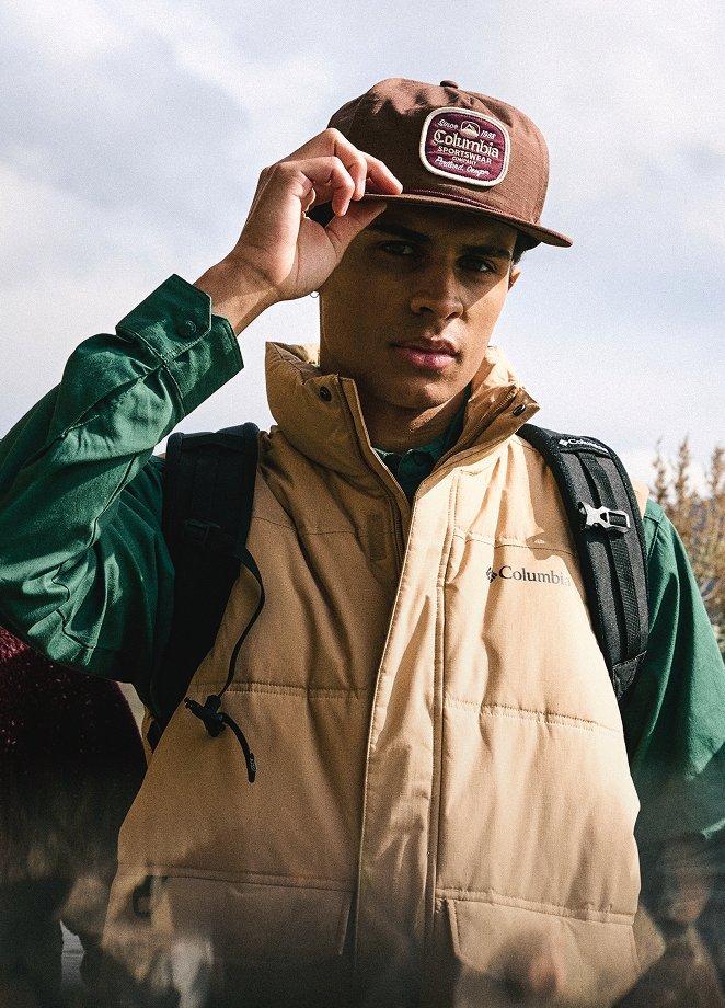 A man hiking on a cloudy day wearing a hat and vest.