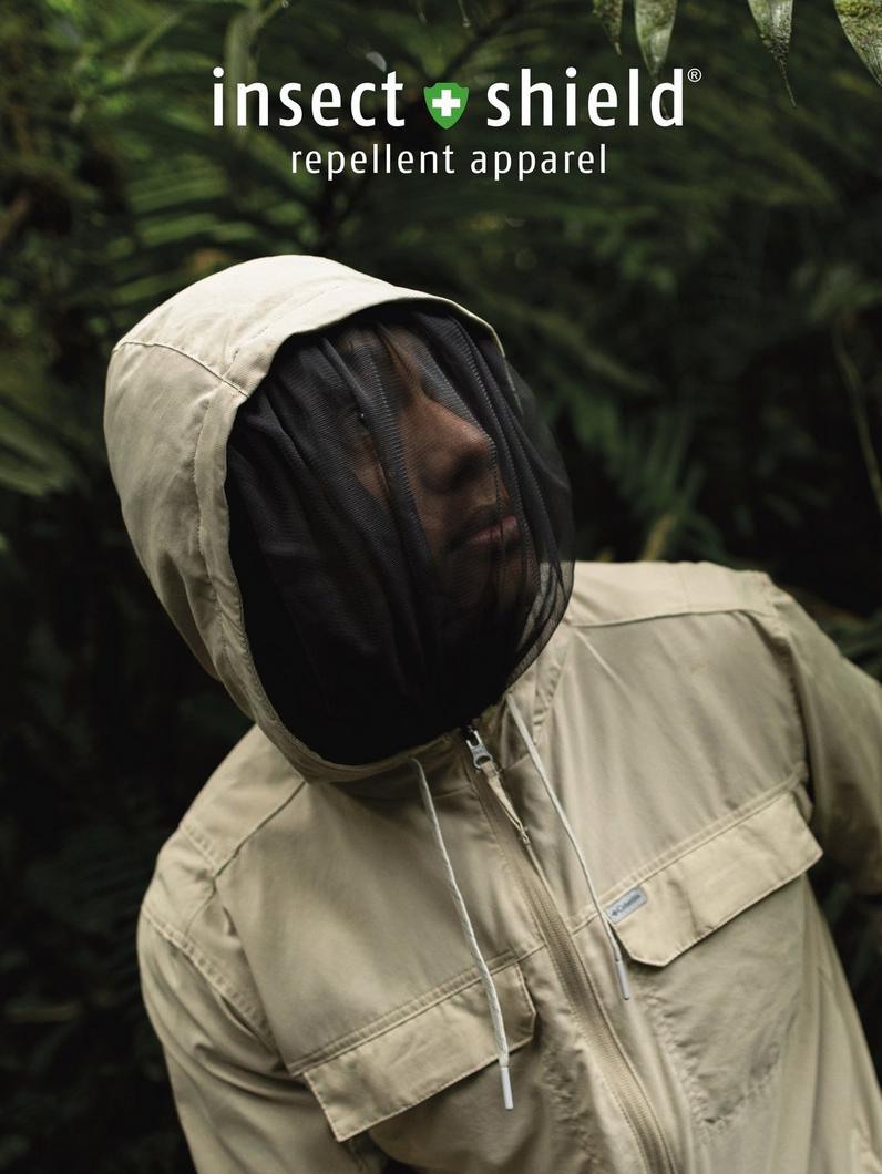 Person wearing tan insect repellent jacket with hood and mesh face protection in outdoor setting.