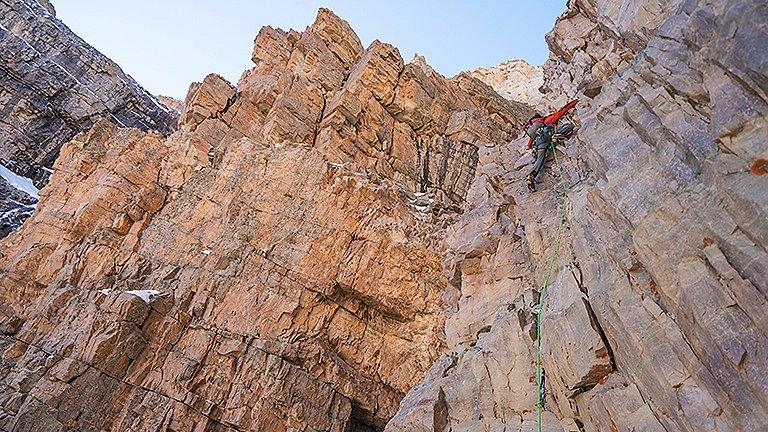 A climber is halfway up a mixed rock and ice route.