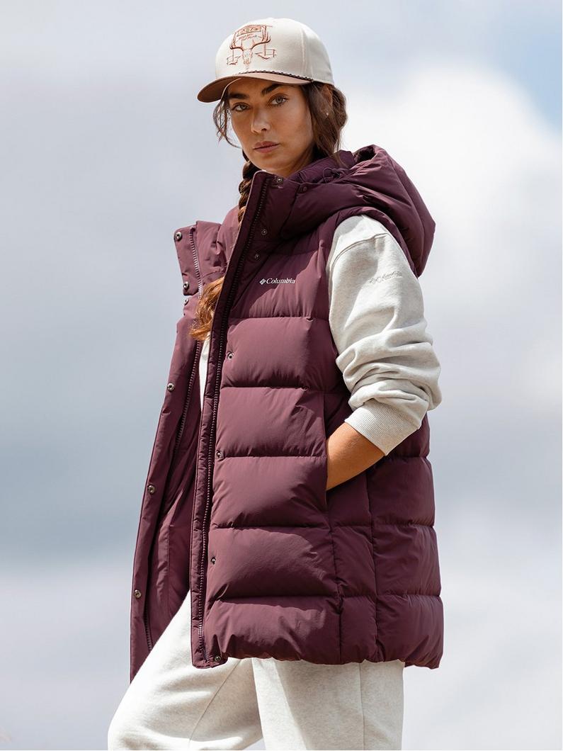 Woman wearing burgundy hooded puffer vest over cream hoodie and sweatpants with embroidered baseball cap.