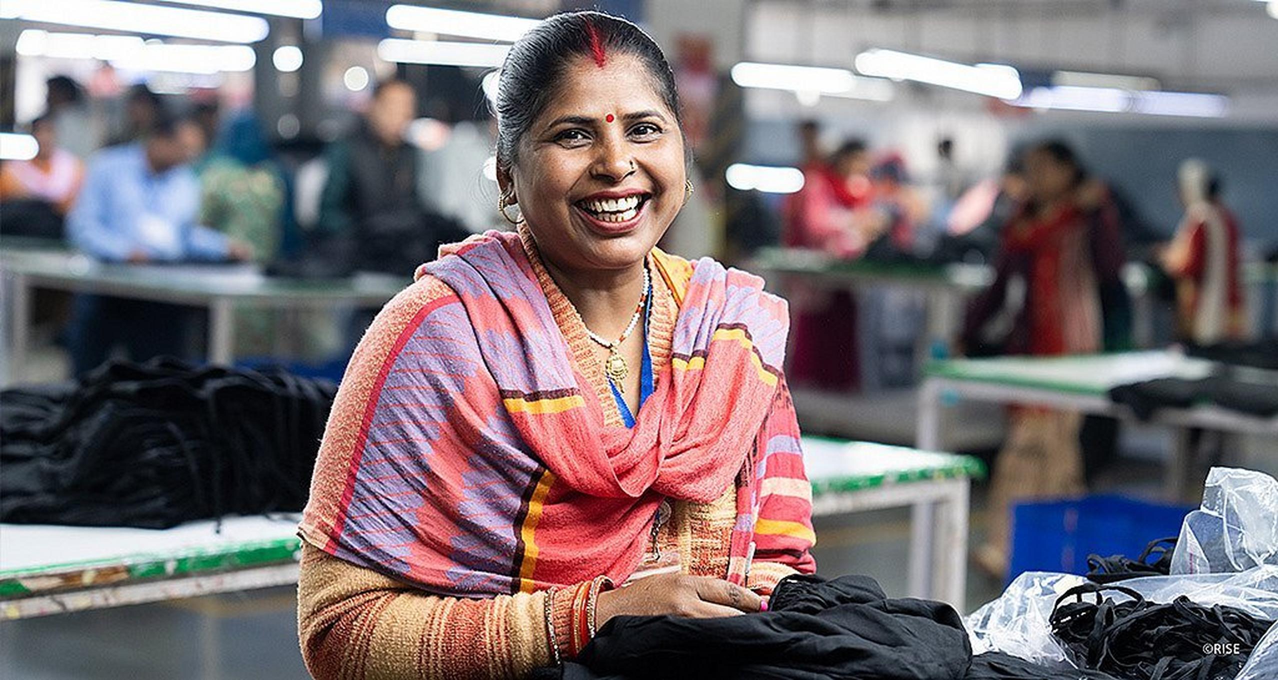 Woman smiling and working on a piece of clothing in a factory