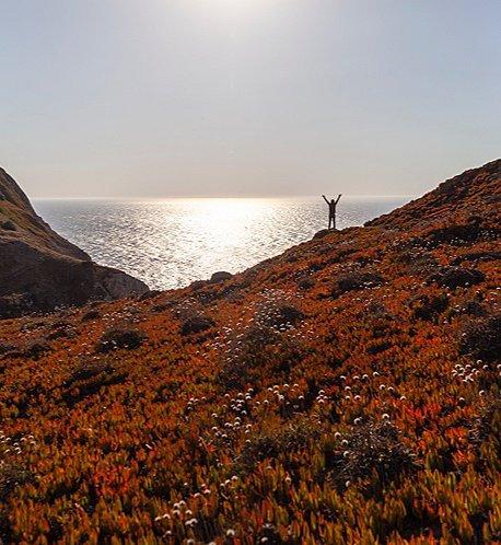 A person standing on a large bluff overlooking the sea.
