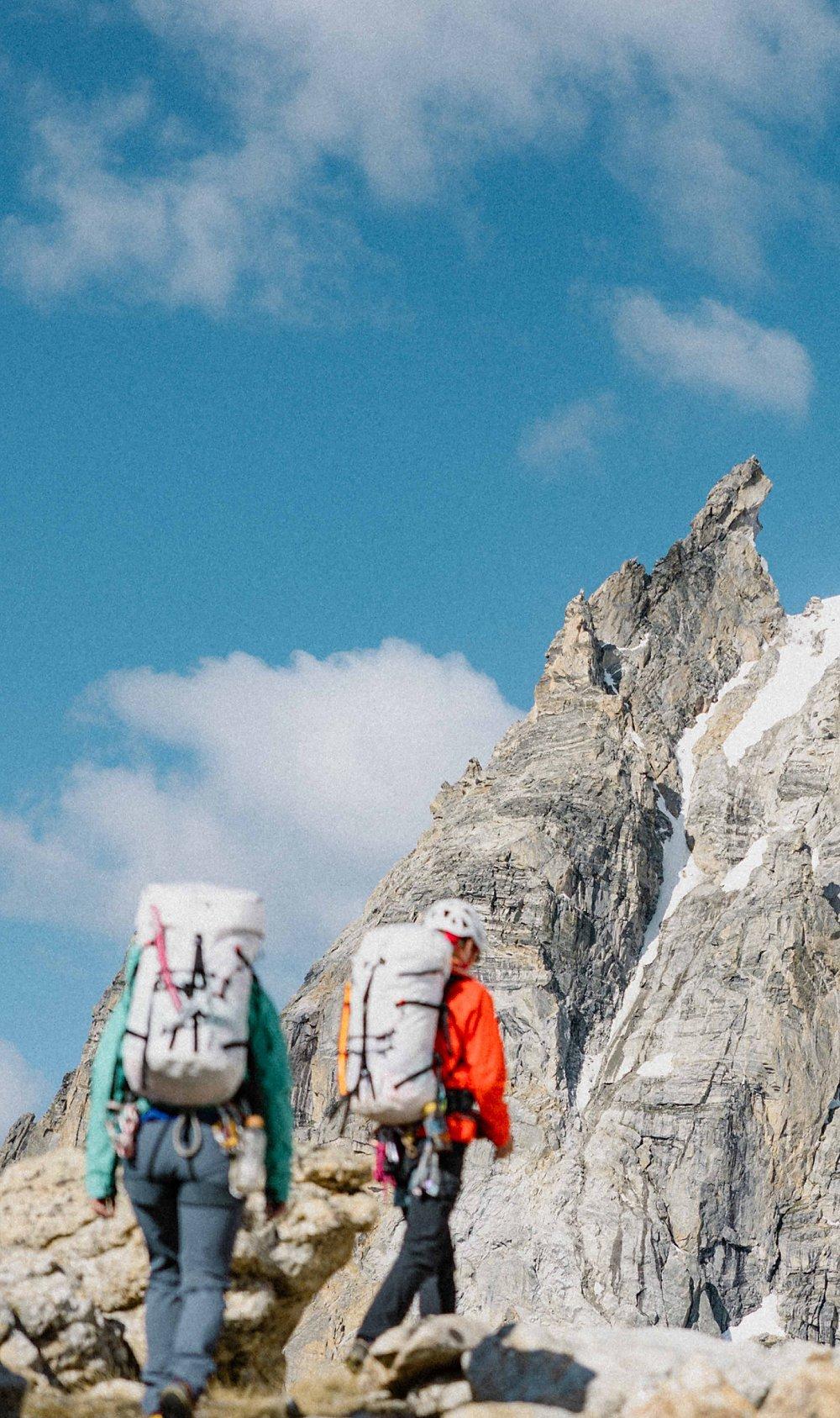 Two alpine climbers make their approach to climb the rock face ahead.