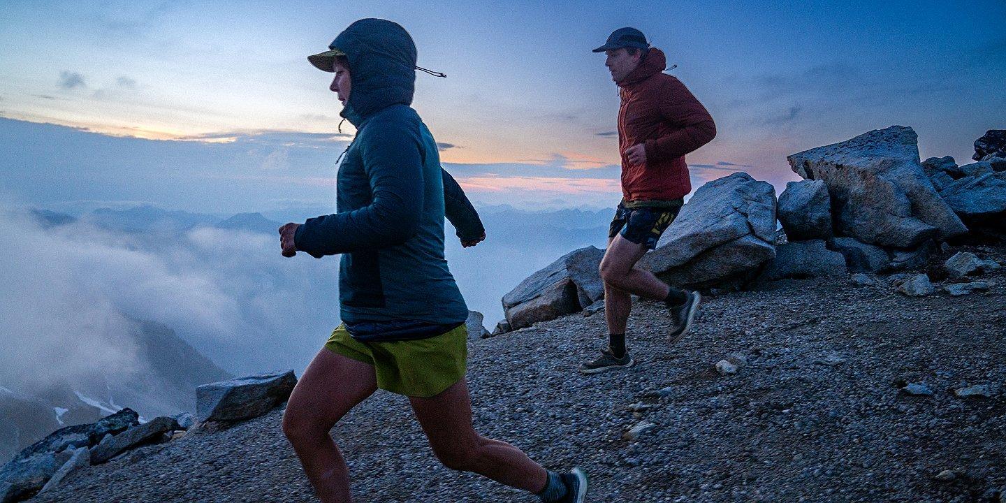 Two runners trail running in the Kor AirShell Hybrid above the colds at sunrise.