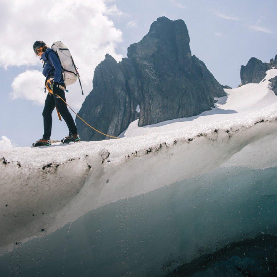 A helmeted mountaineer in crampons descends across ice with the Alpine Light™ Roll Top 45L Backpack.

