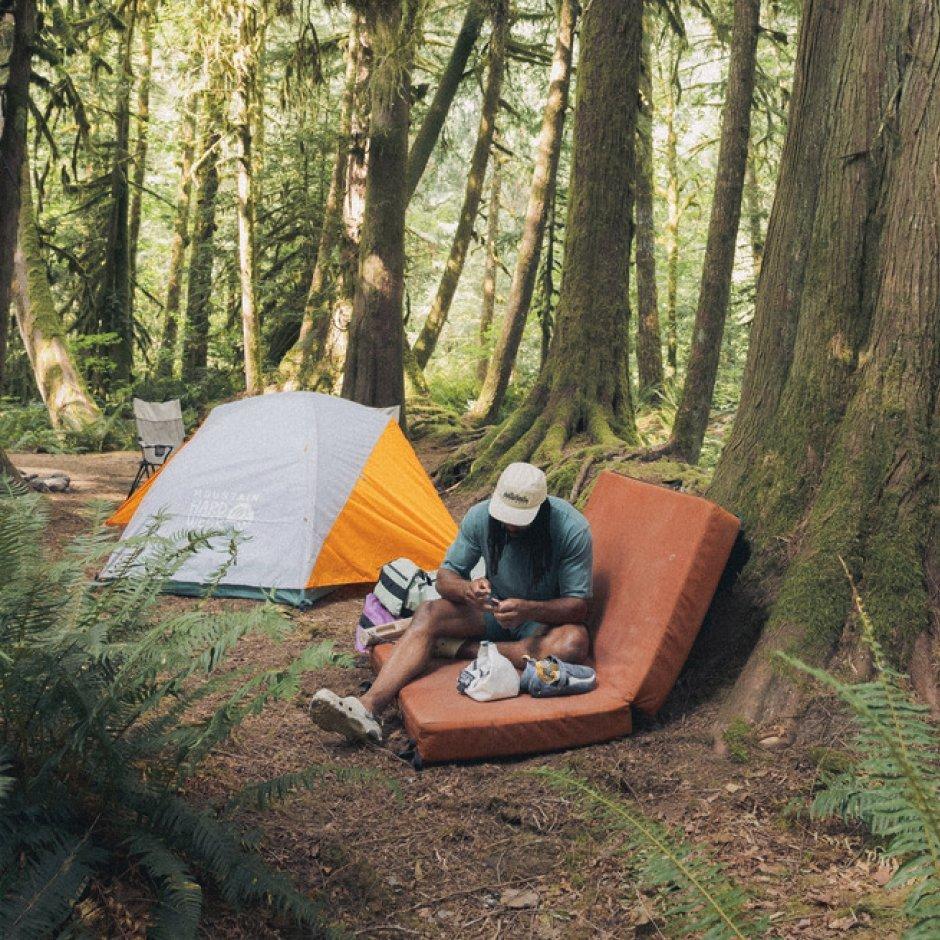 By a Mineral King™ 2 All Season Tent in a grove of trees, a climber seated on a crash pad prepares his gear.