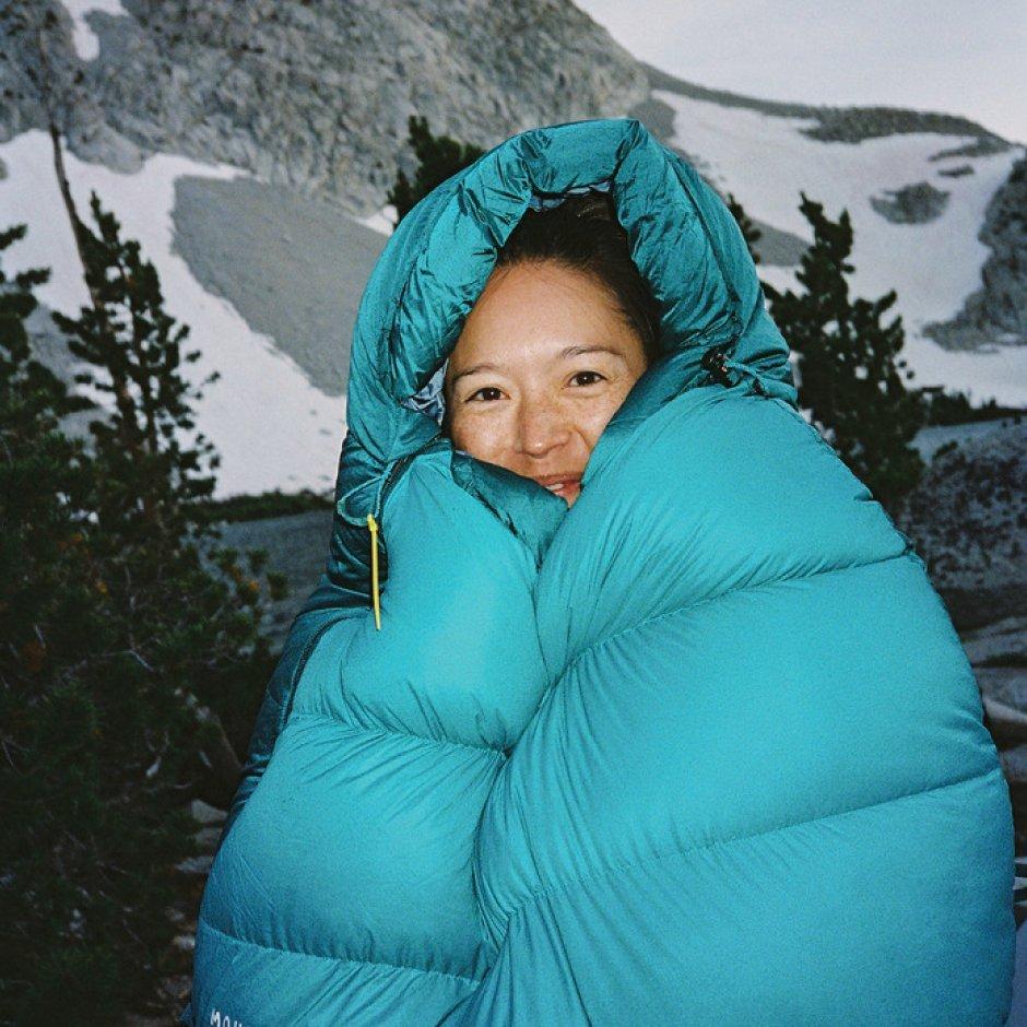 Inside of a Bishop Pass™ 15F/-9C Sleeping Bag, a woman stands with snowy mountains behind her.

