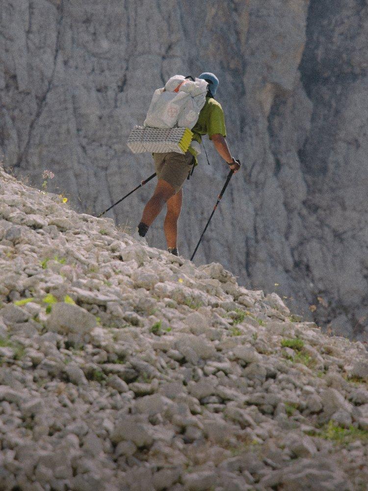 A person with a fully loaded Alakazam™ Backpack and hiking poles treks away across scree

